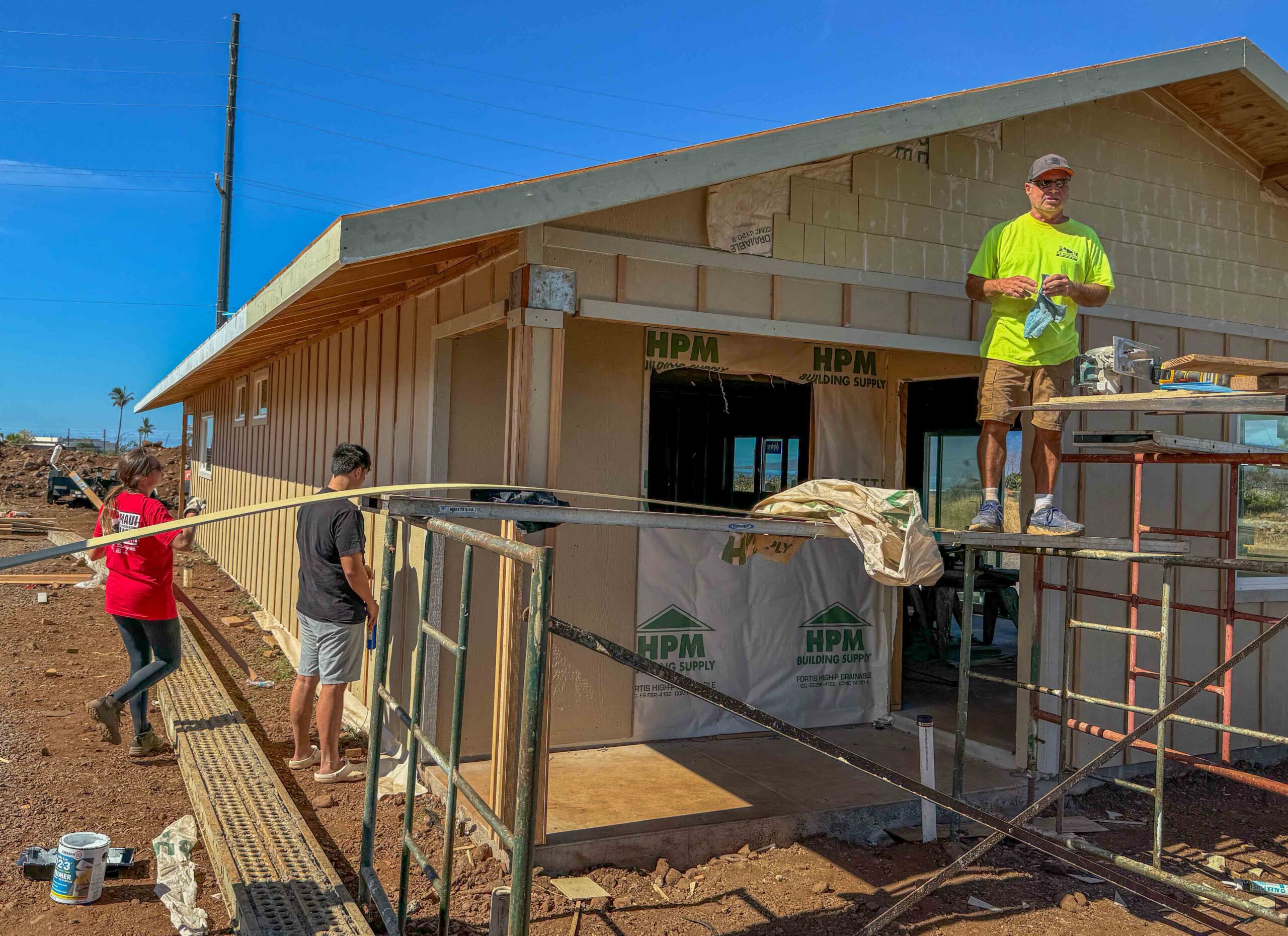 Ariel Ah Hee paints the roof siding as her nephew Kainalu Ah Hee caulks the siding and Derrick Montalvo stands on scaffolding. The family is providing the work force to rebuild their home that was destroyed in the Aug. 8, 2023, fire.